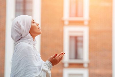 Islamic woman praying outdoor. White hijab. Side view